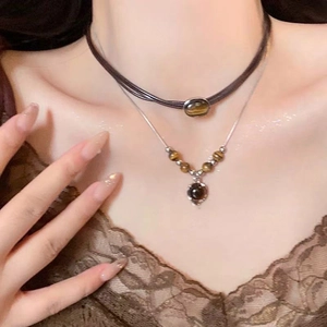 Close-up of layered vintage necklaces with tiger eye stone and beaded pendants on neck
