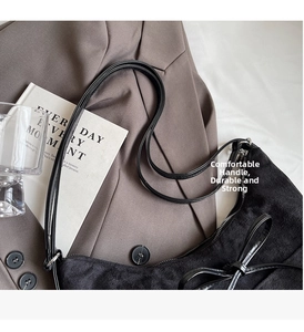 Detail of black suede shoulder bag with bow detail next to blazer and books