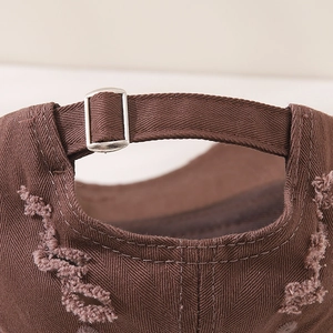 Detailed close-up of distressed cotton twill and metal buckle on dark brown baseball cap