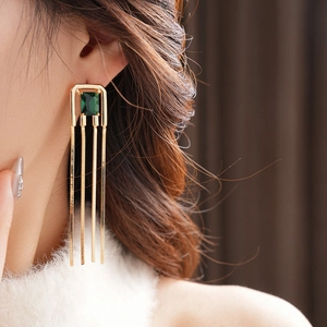 Close-up of vintage gold tassel earrings with square green zircon stones on model