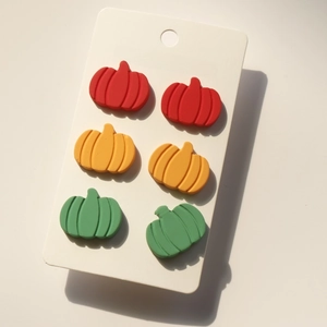 Detailed view of pumpkin-shaped studs in red, orange, and green on a jewelry card