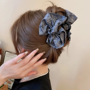 Detail view of a large dark grey fabric hair claw clip with bow prints on a high bun