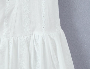 Close-up of white dress with vertical floral embroidery and pleated waist detail