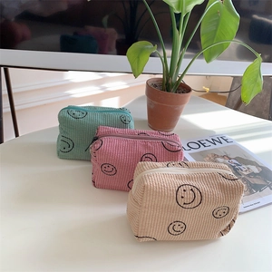 Three corduroy smiley face cosmetic bags in pastel colors shown on a white table