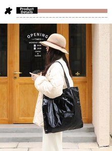 Black glossy nylon tote bag with a soft wrinkled texture shown in a casual outdoor setting