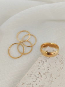 Detailed view of one wide and four thin gold minimalist stacking rings on a stone prop