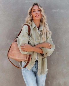Detailed close-up of distressed light olive green denim jacket texture with frayed edges