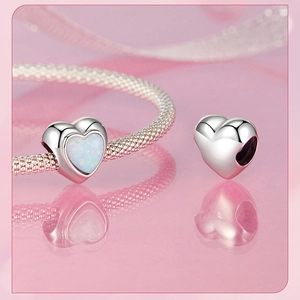 Detailed macro view of silver heart charms with blue opal inlay on pink ribbon background