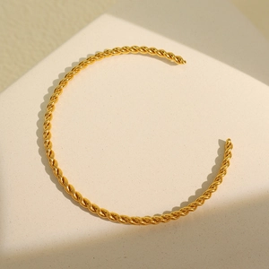 Minimalist gold twisted cable open cuff bracelet on a textured geometric stand