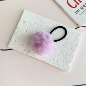 Close-up of light purple plush pom-pom hair tie on a white stone display plate