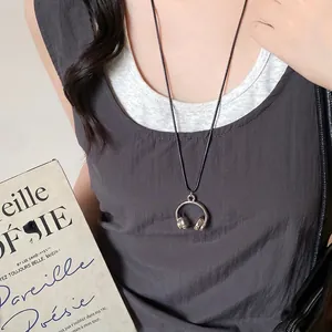 Gros plan d'un collier pendentif casque argenté porté par un mannequin au style minimaliste