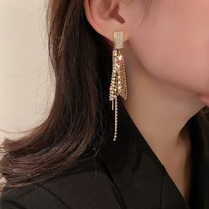 Detail showing long golden tassel earrings with sequins on a model wearing a black blazer