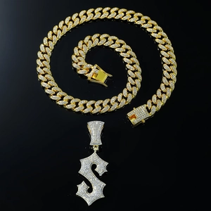 Macro detail of iced-out Cuban chain and gold S-letter pendant with sparkling rhinestones