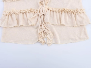 Detail of beige knit top featuring ruffle edges and delicate front tie-up closure