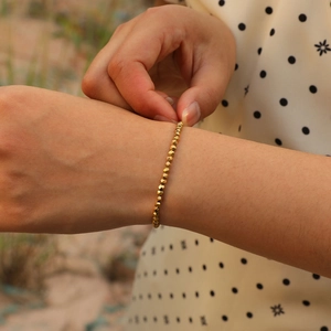 Detailed view of women wearing a gold faceted hematite beaded bracelet on wrist