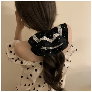 Close-up of a large black polka dot scrunchie with white lace trim on model hair