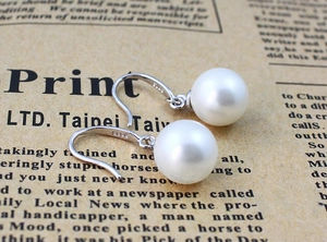 Detail of S925 silver hook earrings with glossy white round pearls on newspaper