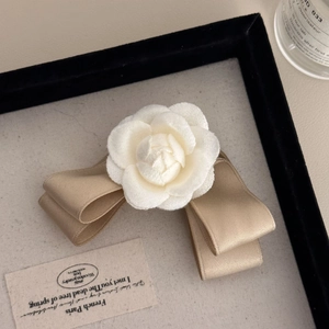 Detail of white camellia fabric flower and champagne satin bow on a vintage hair clip