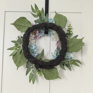 Detail of autumn hydrangea wreath with green leaves and blue flowers on white door