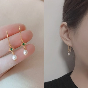 Detailed view of elegant gold-plated drop earrings with green zircon and white pearl