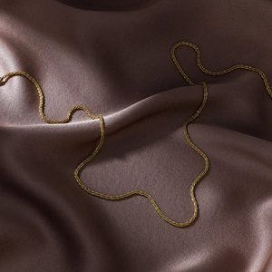 Vue macro d'une chaîne dorée fine à texture raffinée sur tissu en soie marron