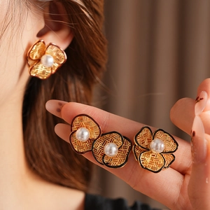 Detail of flower stud earrings with woven gold texture, white pearl, and black enamel edge