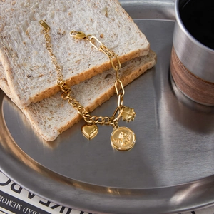 Detailed shot of a gold coin bracelet with heart and clover charms on a metal tray
