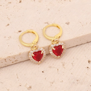 Detail of gold heart earrings with red crystal and white zircon on stone background