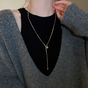 Detail of gold-plated square zircon necklace with ball pendant on a grey cardigan model