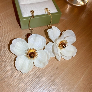 Elegant white mesh flower earrings with gold stamens on a natural wooden background