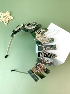 Macro detail of raw green crystal crown with silver moon, sun, and snake pendants