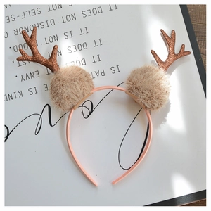 Detail of brown glitter antlers with fluffy beige pom-poms on a pink Christmas headband