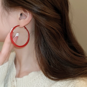 Close-up of oversized red hoop earrings in glossy metal finish worn by model