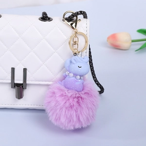 Detail of purple unicorn plush ball keychain hanging on a white quilted bag