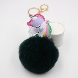 Detail view of colorful unicorn keychain with fluffy dark green pompom and gold metal ring