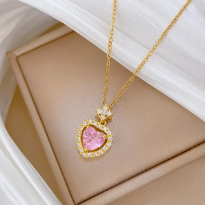 Close-up of a pink heart pendant on a gold titanium necklace over white silk