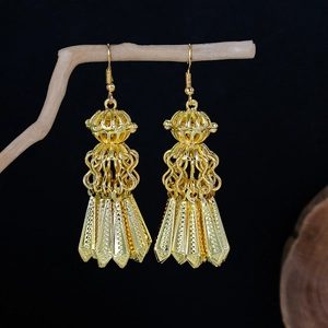 Close-up of bohemian gold peacock earrings with bell tassels on a wooden branch