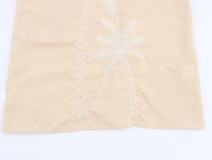 Detail von besticktem Palmenmuster und Holzperlen am beigefarbenen Boho-Maxikleid