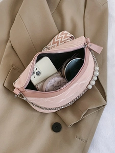 Pink crescent crossbody bag with pleated texture and pearl chain strap on beige blazer