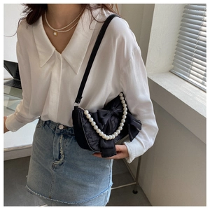 Detail of black satin bow handbag featuring a decorative pearl handle and stylish texture