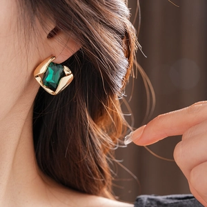Nahaufnahme eines goldenen geometrischen Ohrrings mit grünem Edelstein am Modellohr