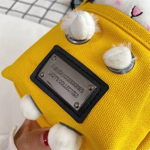 Close-up of bright yellow canvas bag featuring plush white balls and metal logo plate