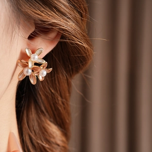 Close-up of gold-plated flower earrings with pearls worn by a model in soft lighting