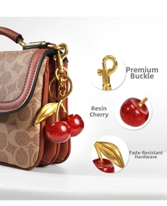 Detail of red cherry bag charm with golden leaves on a patterned shoulder strap