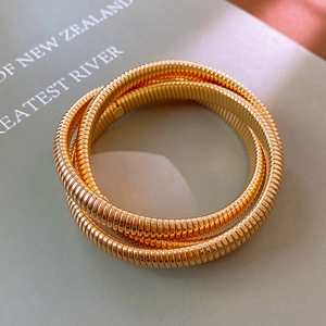 Détail d'un bracelet Tubogas à trois couches en acier inoxydable doré sur un livre