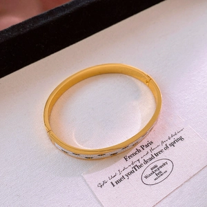 Détail du bracelet émaillé doré avec des charmes d'œil bleu sur tissu blanc