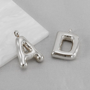 Polished silver stainless steel puffy bubble letter A and D pendants on grey fabric