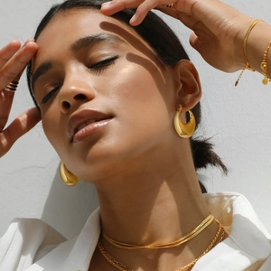 Model wearing gold chunky teardrop earrings and layered chain necklaces in natural sunlight