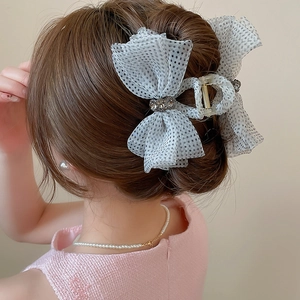Detailed view of a white polka dot mesh bow hair claw clip with rhinestones on a bun