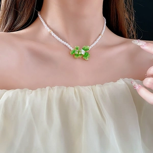 Close-up of a pearl necklace featuring a green gemstone bow pendant on a model neck